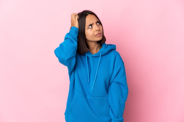Young latin woman isolated on pink background having doubts while scratching head