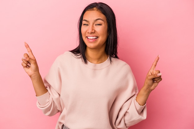 Young latin woman isolated on pink background  indicates with both fore fingers up showing a blank space.