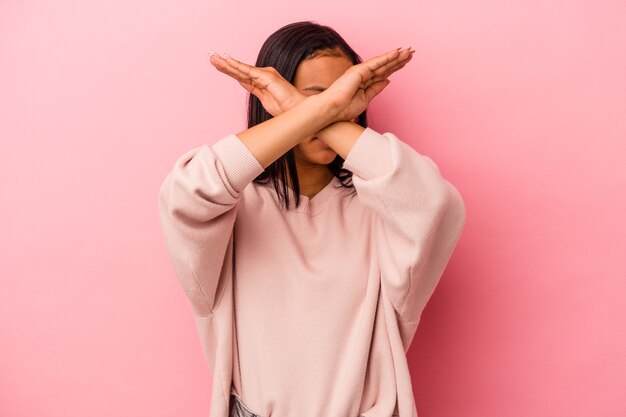 Young latin woman isolated on pink background  keeping two arms crossed, denial concept.