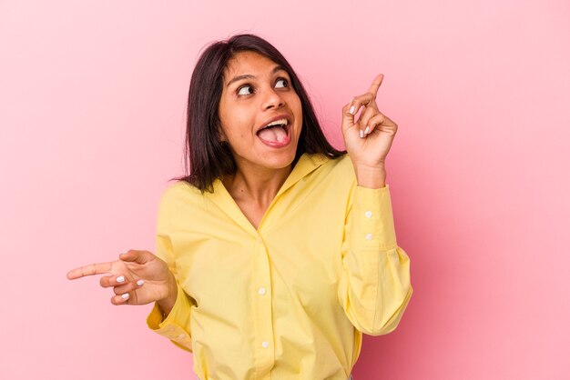 Young latin woman isolated on pink background pointing to different copy spaces, choosing one of them, showing with finger.