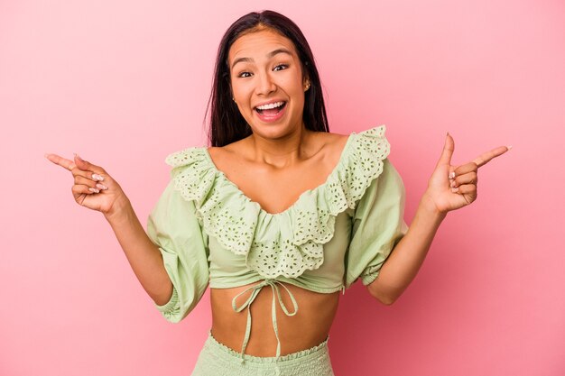 Young latin woman isolated on pink background  pointing to different copy spaces, choosing one of them, showing with finger.