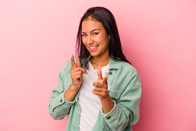 指で正面を指しているピンクの背景に分離された若いラテン女性。
