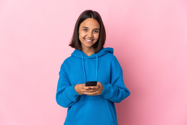 モバイルでメッセージを送信するピンクの背景に分離された若いラテン女性