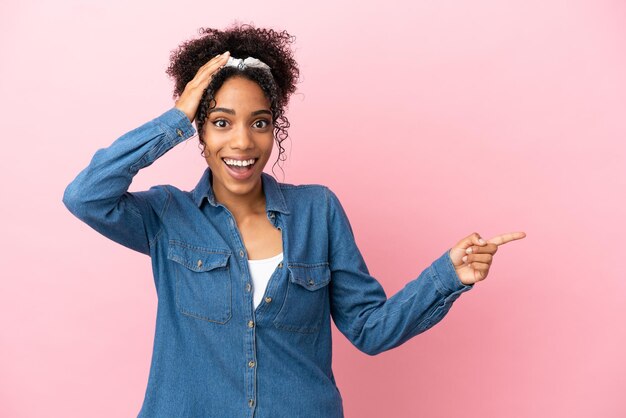 Young latin woman isolated on pink background surprised and pointing finger to the side