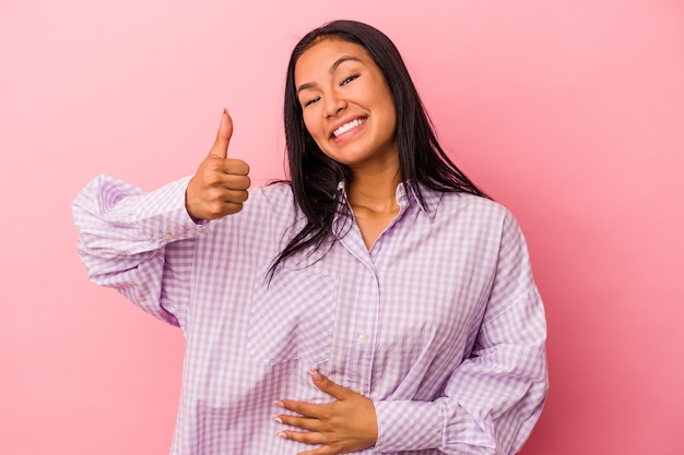Young latin woman isolated on pink background  touches tummy, smiles gently, eating and satisfaction concept.
