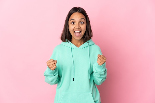 Young latin woman isolated on pink wall celebrating a victory in winner position