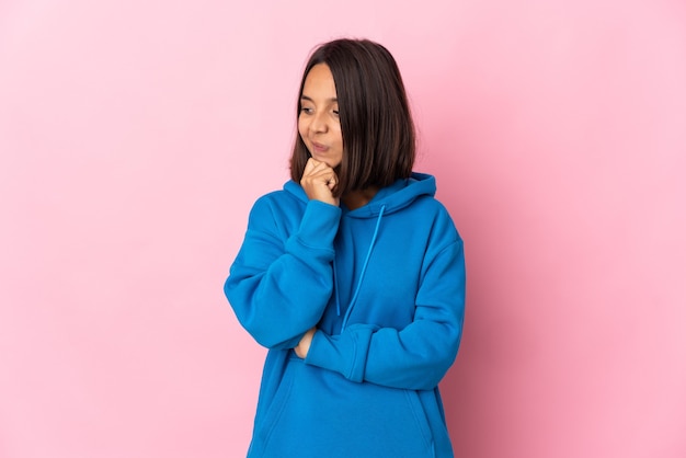 Young latin woman isolated on pink wall looking to the side and smiling