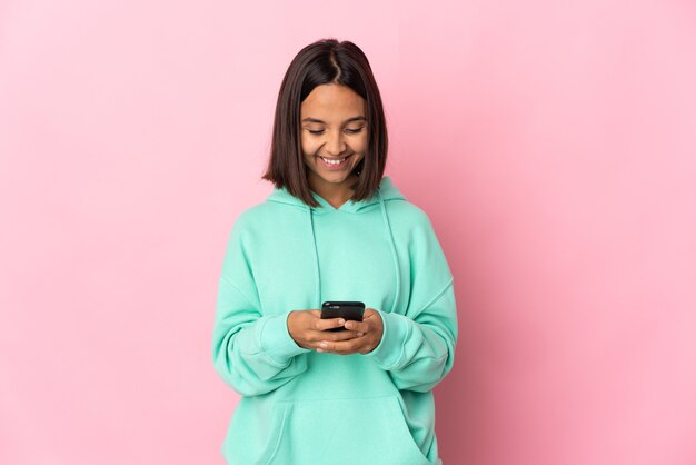 Young latin woman isolated on pink wall sending a message with the mobile