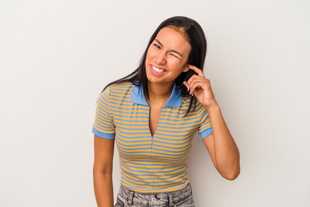 Young latin woman isolated on white background  covering ears with fingers, stressed and desperate by a loudly ambient.