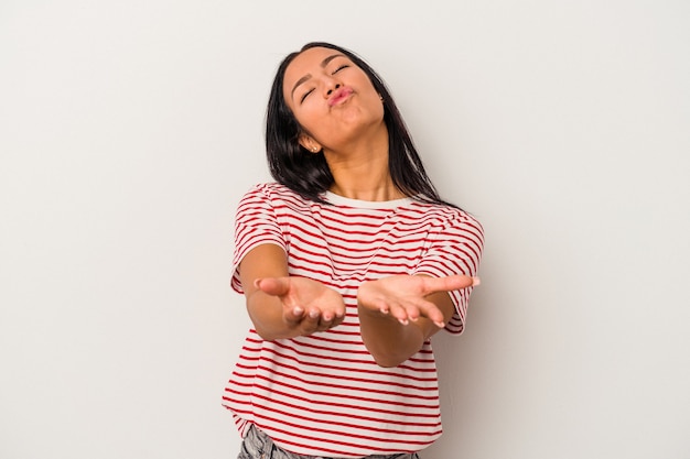 Young latin woman isolated on white background  folding lips and holding palms to send air kiss.