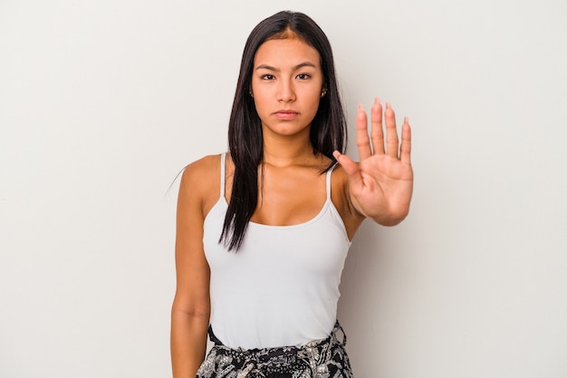 一時停止の標識を示す伸ばした手で立っている白い背景で隔離の若いラテン女性は、あなたを防ぎます。