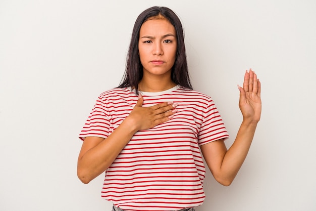 Young latin woman isolated on white background  taking an oath, putting hand on chest.