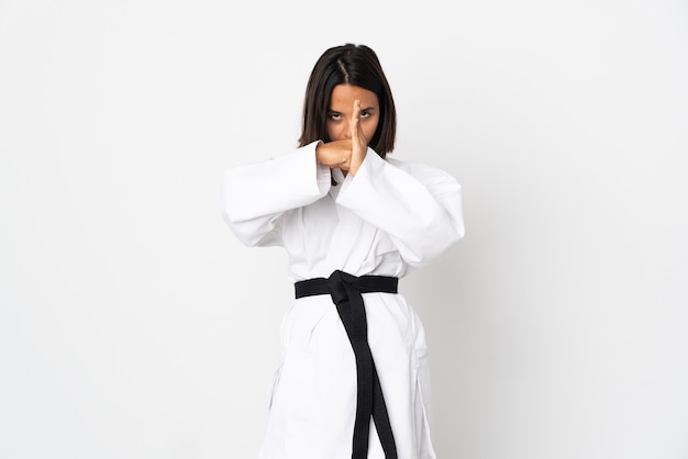 Young latin woman isolated on white wall doing karate and saluting