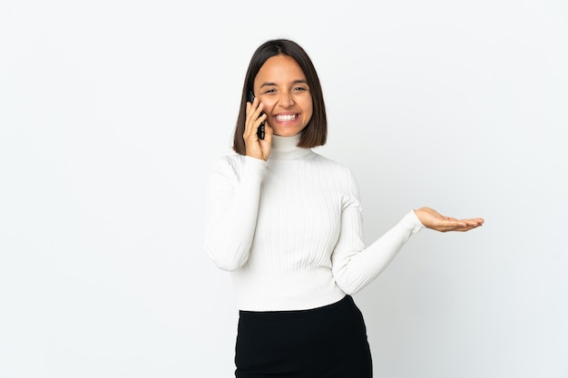 Young latin woman isolated on white wall keeping a conversation with the mobile phone with someone