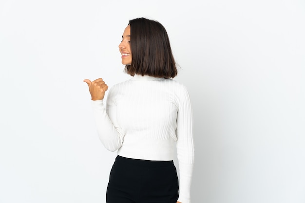 Молодая латинская женщина изолирована на белой стене, указывая в сторону, чтобы представить продукт