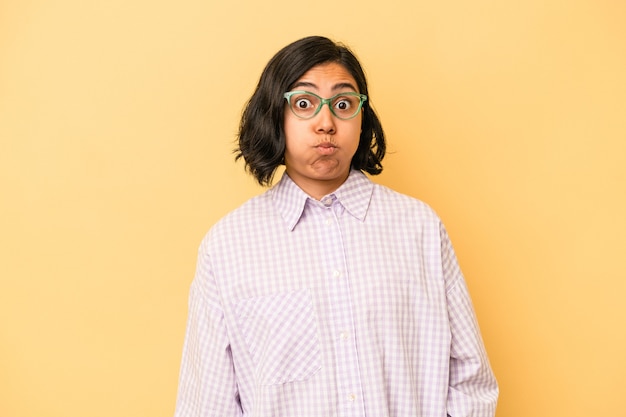 Young latin woman isolated on yellow background blows cheeks, has tired expression. Facial expression concept.