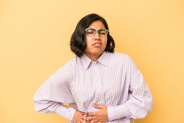 Young latin woman isolated on yellow background having a liver pain, stomach ache.