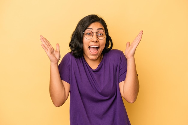 Young latin woman isolated on yellow background holding something little with forefingers, smiling and confident.