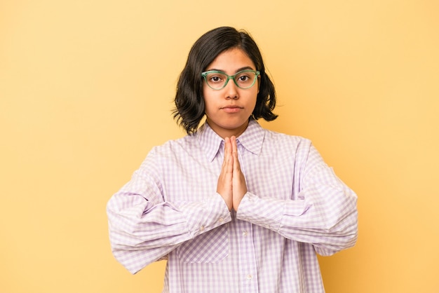 Young latin woman isolated on yellow background praying, showing devotion, religious person looking for divine inspiration.