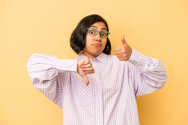 Young latin woman isolated on yellow background showing thumbs up and thumbs down, difficult choose concept