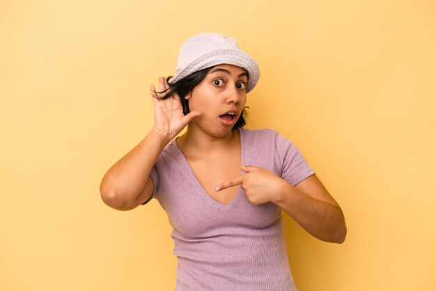 Young latin woman isolated on yellow background trying to listening a gossip.