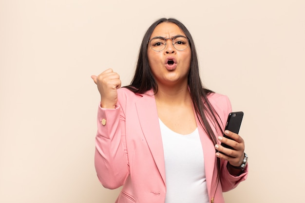 Young latin woman looking astonished in disbelief, pointing at object on the side and saying wow, unbelievable