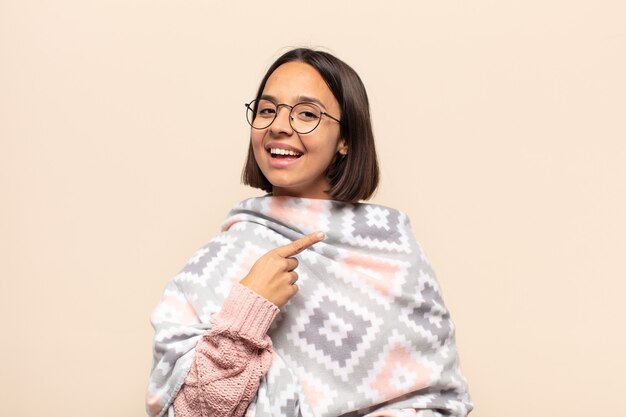 Young latin woman looking excited and surprised pointing to the side and upwards to copy space