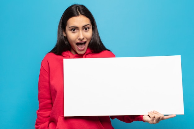 Young latin woman looking happy and pleasantly surprised, excited with a fascinated and shocked expression