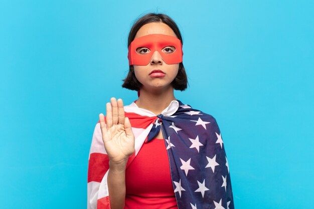 Young latin woman looking serious, stern, displeased and angry showing open palm making stop gesture