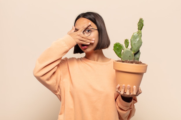 Young latin woman looking shocked, scared or terrified, covering face with hand and peeking between fingers