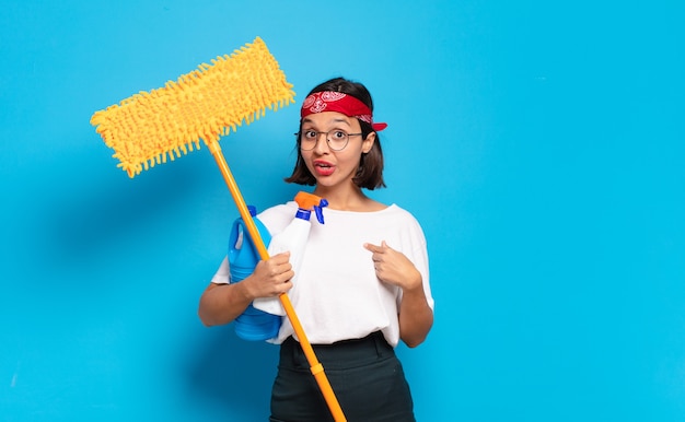 Young latin woman looking shocked and surprised with mouth wide open, pointing to self