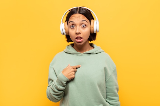 Young latin woman looking shocked and surprised with mouth wide open, pointing to self