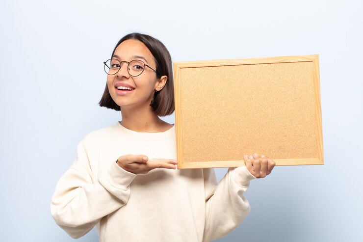 Photo young latin woman looking surprised and shocked, with jaw dropped holding an object with an open hand on the side