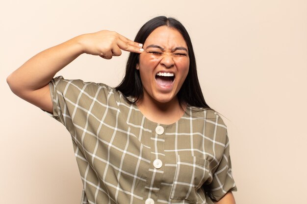 Young latin woman looking unhappy and stressed, suicide gesture making gun sign with hand, pointing to head