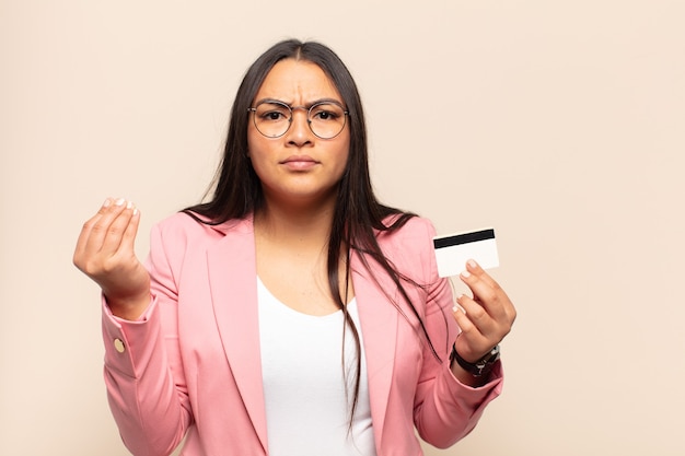 Young latin woman making capice or money gesture, telling you to pay your debts!