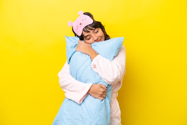 Young latin woman in pajamas isolated on yellow background