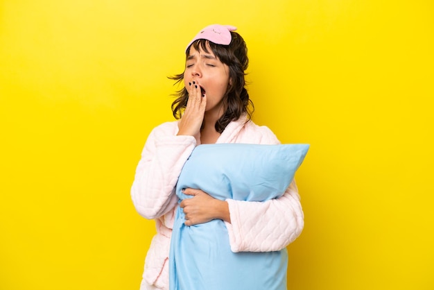 Young latin woman in pajamas isolated on yellow background