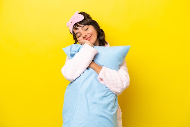 Young latin woman in pajamas isolated on yellow background