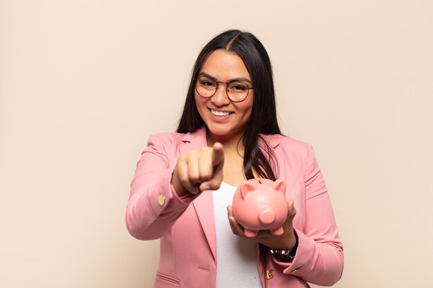 Young latin woman pointing at camera with a satisfied, confident, friendly smile, choosing you