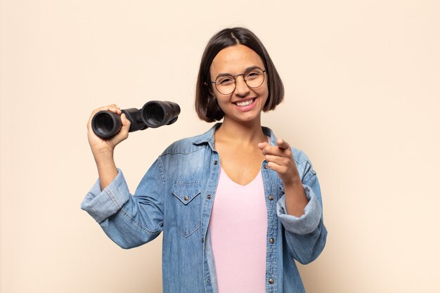 Young latin woman pointing at camera with a satisfied, confident, friendly smile, choosing you