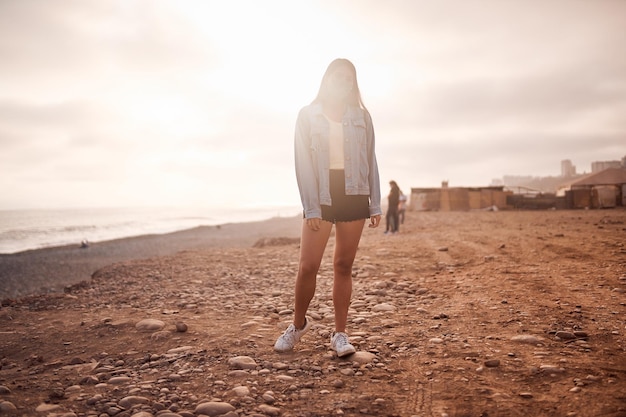 Молодая латинская женщина позирует, идя по песку во время красивого заката