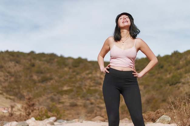 Young latin woman posing standing smiling with eyes closed and hands on hips in an arid valley