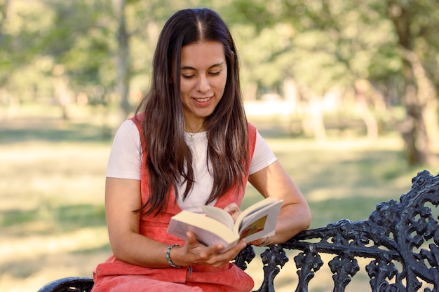 屋外で勉強している公園のベンチに座って本を読んで若いラテン女性