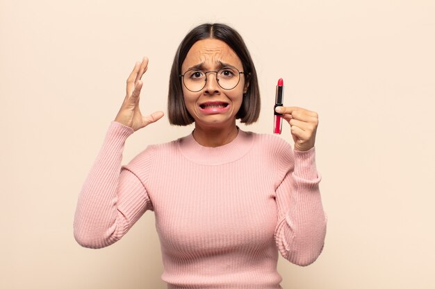 Young latin woman screaming with hands up in the air, feeling furious, frustrated, stressed and upset