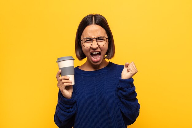 Young latin woman shouting aggressively with an angry expression or with fists clenched celebrating success