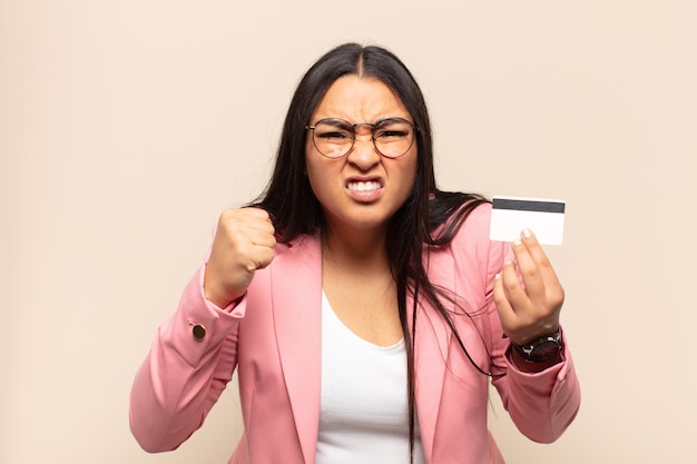 Young latin woman shouting aggressively with an angry expression or with fists clenched celebrating success
