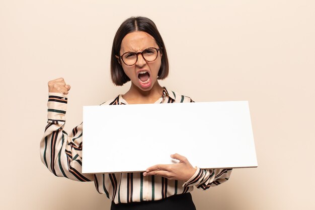 Young latin woman shouting aggressively with an angry expression or with fists clenched celebrating success