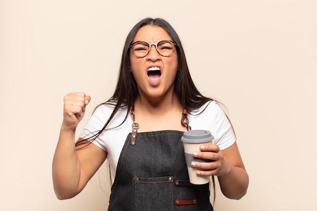 Young latin woman shouting aggressively with an angry expression or with fists clenched celebrating success