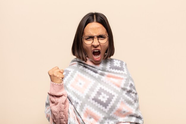 Young latin woman shouting aggressively with an angry expression or with fists clenched celebrating success