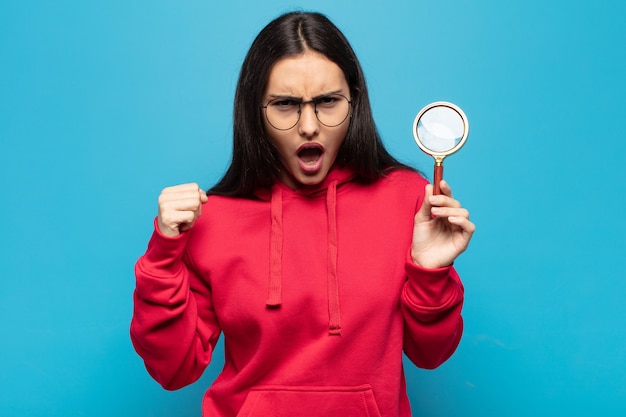 Young latin woman shouting aggressively with an angry expression or with fists clenched celebrating success